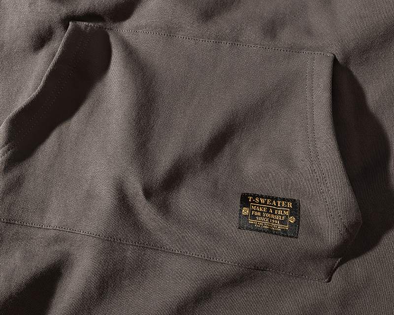 Close-up of solid color kangaroo pocket on warm round neck sweatshirt in cotton and polyester blend, featuring label detail.